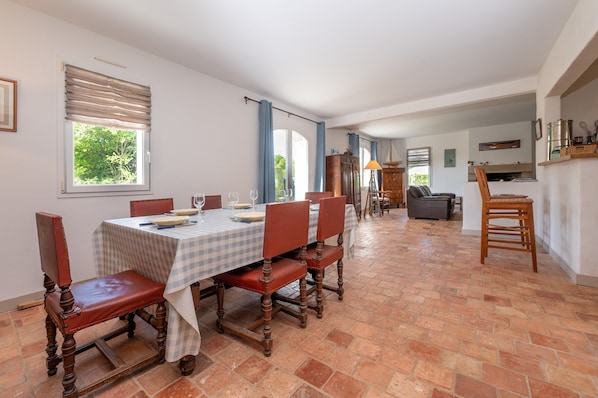 A dining area with a table set for six, wooden chairs, and a kitchen in the background.
