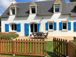 A white building with blue shutters, a wooden fence, and a patio with a table and chairs.