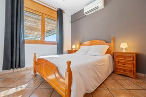 Une chambre à coucher avec un lit en bois, une table de chevet avec une lampe, une fenêtre avec des rideaux et un appareil de climatisation.