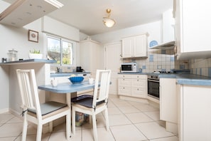 A kitchen with white cabinets, a blue countertop, a dining table with chairs, a microwave, an oven, and a window. - Serene Getaway Steps from the Carnac Alignments – Vacation Home (Carnac)