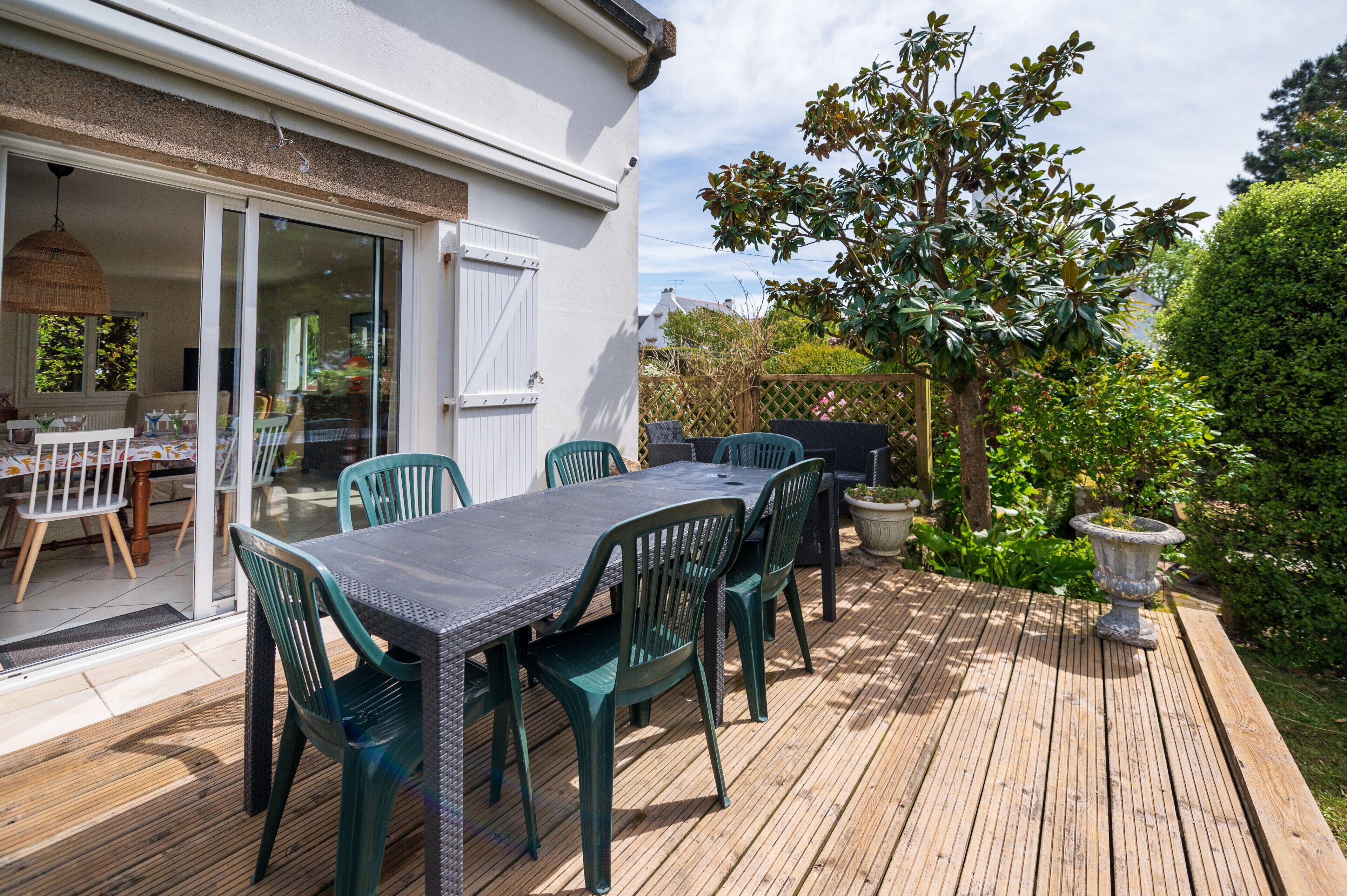 An outdoor patio with a table and chairs, a sliding glass door leading to an interior dining area, and a well-maintained garden.