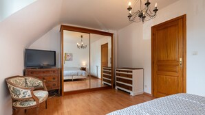 A bedroom with a bed, a television, a dresser, a chair, a wardrobe, and a chandelier.
