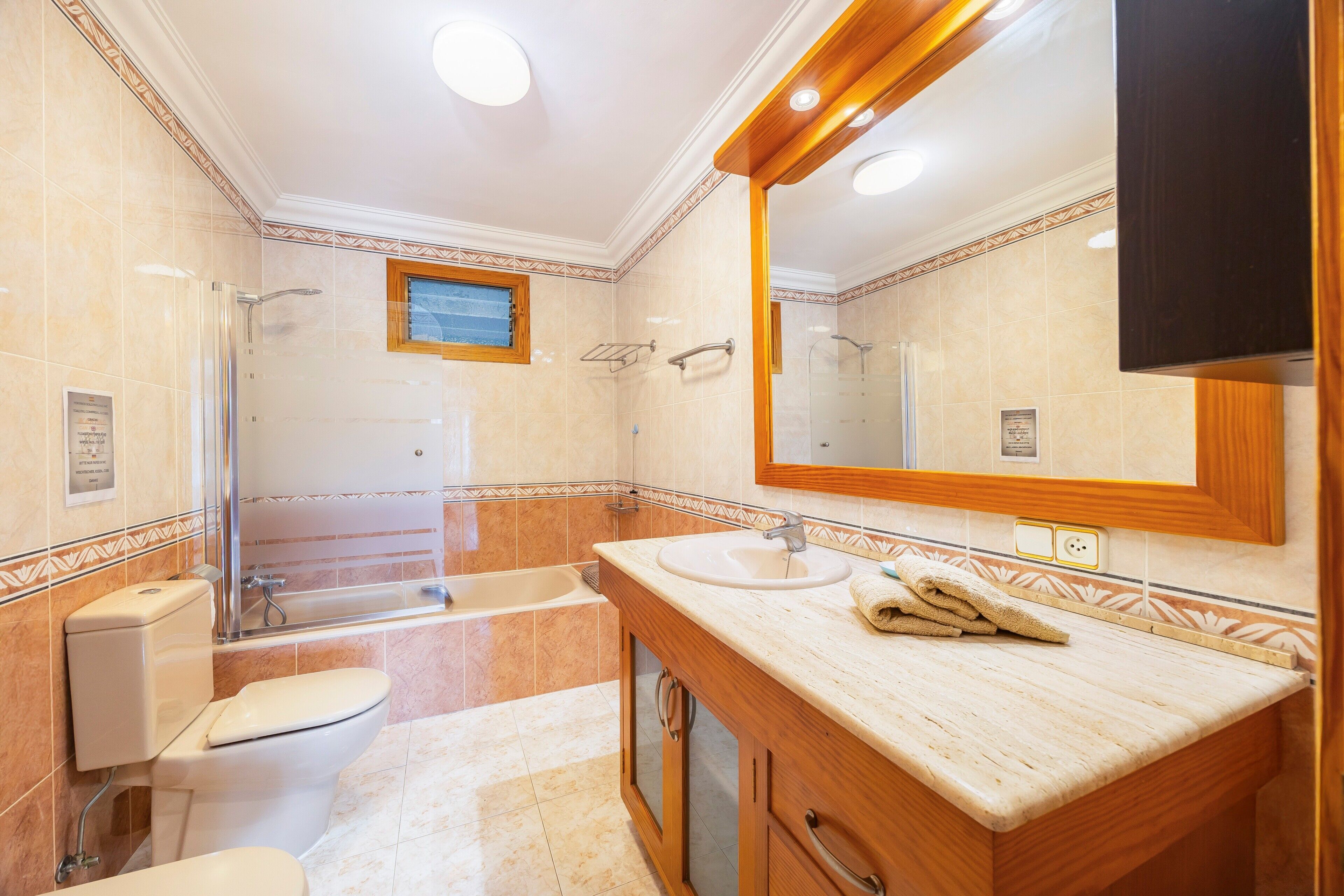 Un baño con ducha, inodoro, lavamanos y un espejo grande.
