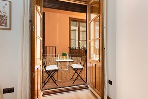 An open door leading to a balcony with two chairs and a small table, a potted plant, and a view of the outside.