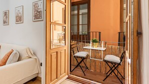 Una stanza con una porta in legno, un divano bianco e un balcone con due sedie e un tavolo.