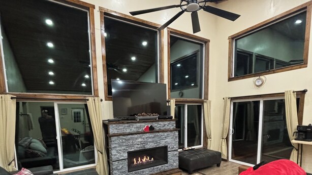 Una sala de estar moderna con chimenea, ventanas amplias y ventilador de techo.