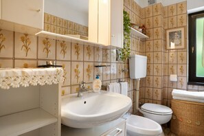 Un baño con lavamanos, inodoro y un estante con artículos de aseo.