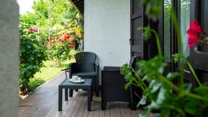 Un patio con mobiliario de mimbre y piso de baldosas, rodeado de vegetación y un sendero de ladrillo.