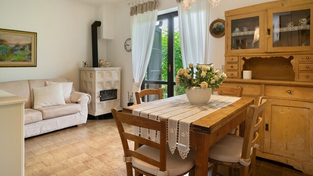 Una cocina acogedora con una mesa de madera, sillas, un jarrón de flores y un armario con puertas de cristal.