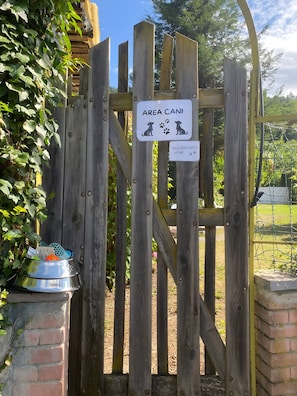 A wooden gate with a sign indicating an area for dogs, a metal bowl with items, and a brick wall.