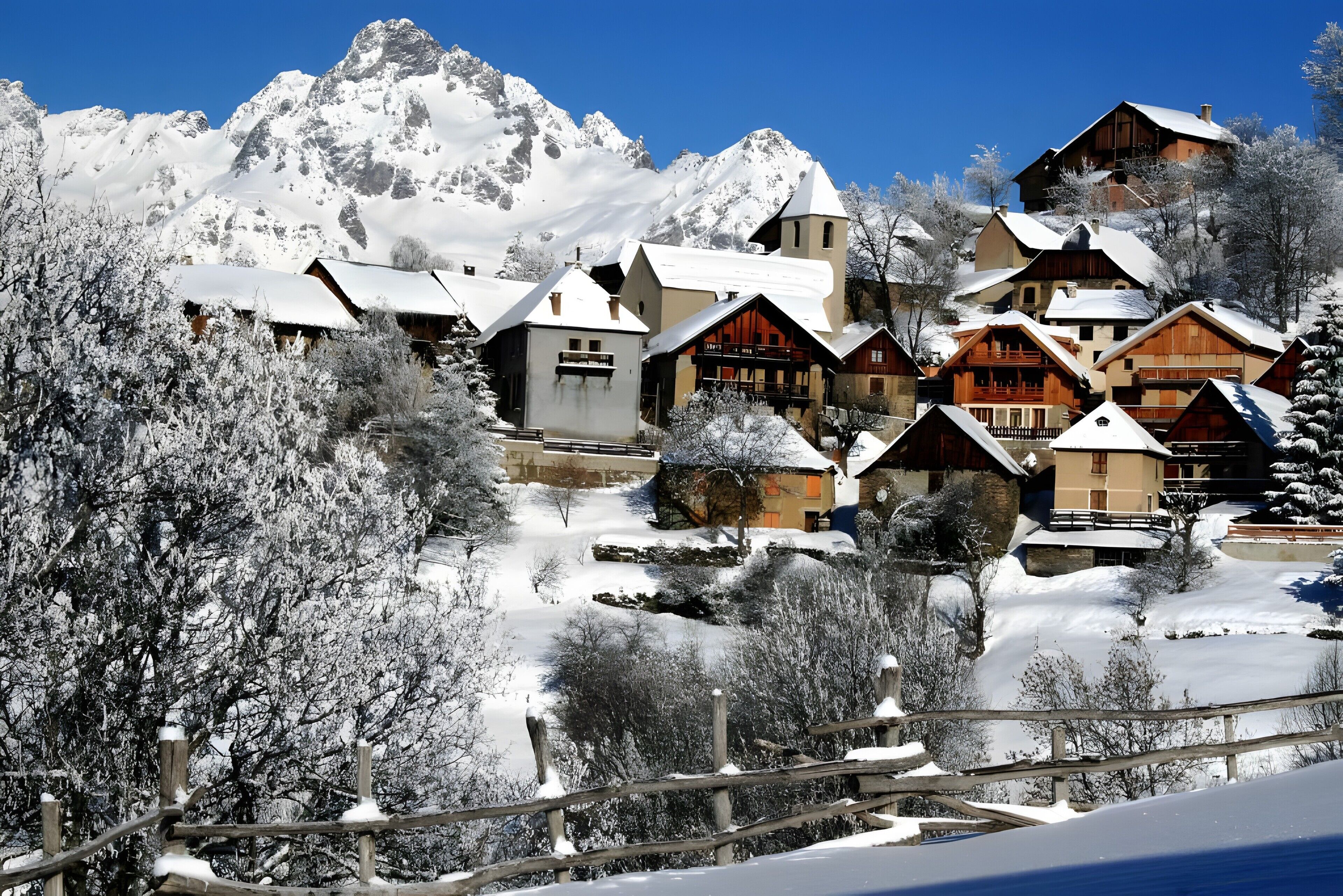 A cluster of wooden chalets with snow-covered roofs, set against a backdrop of snow-capped mountains.
