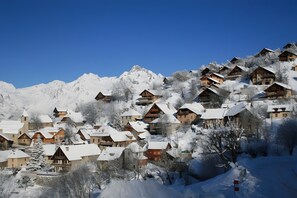 Ein schneebedecktes Dorf mit Holzhäusern, blauem Himmel und einem Berg im Hintergrund.