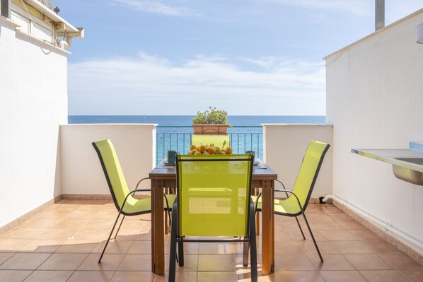 A balcony with a table and chairs, a potted plant, and a view of the sea.