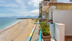 Una vista sulla costa con una spiaggia, un balcone con una pianta in vaso e un edificio con balconi affacciati sul mare.