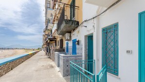 Un vicolo stretto con vista sulla spiaggia, un muro di pietra e edifici con persiane e balconi blu.