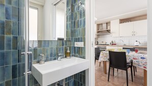 Un bagno con un lavandino bianco, cabina doccia in vetro e parete rivestita di piastrelle.