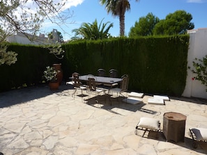 Une terrasse extérieure avec un sol en pierre, une table en métal avec des chaises et un petit tabouret en bois.