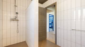 Un baño con paredes de azulejos blancos, una ducha con cabezal de ducha manual y una puerta que da a otra habitación.