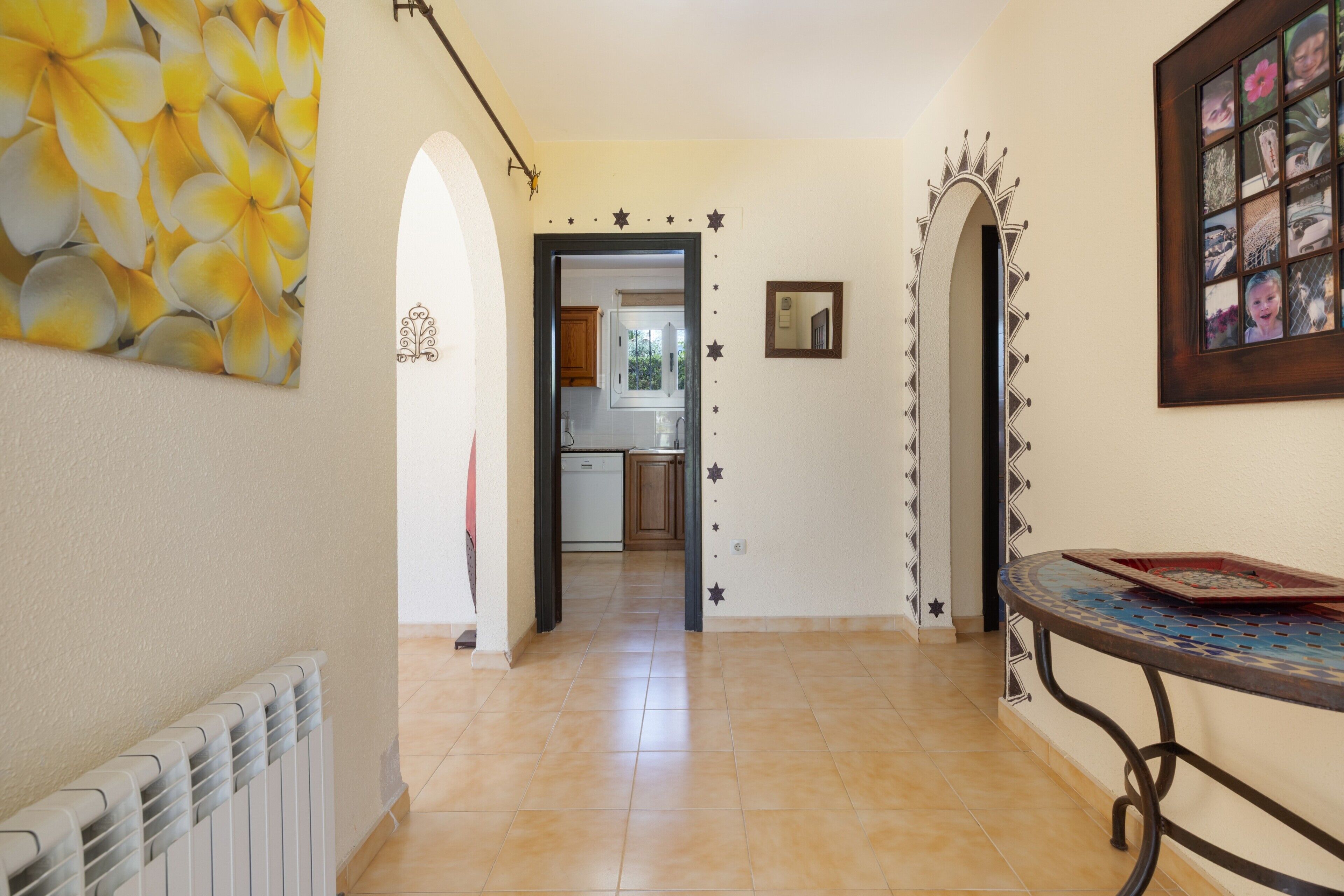 A hallway with a radiator, a table with a tray, a mirror, and a framed photo collage on the wall.