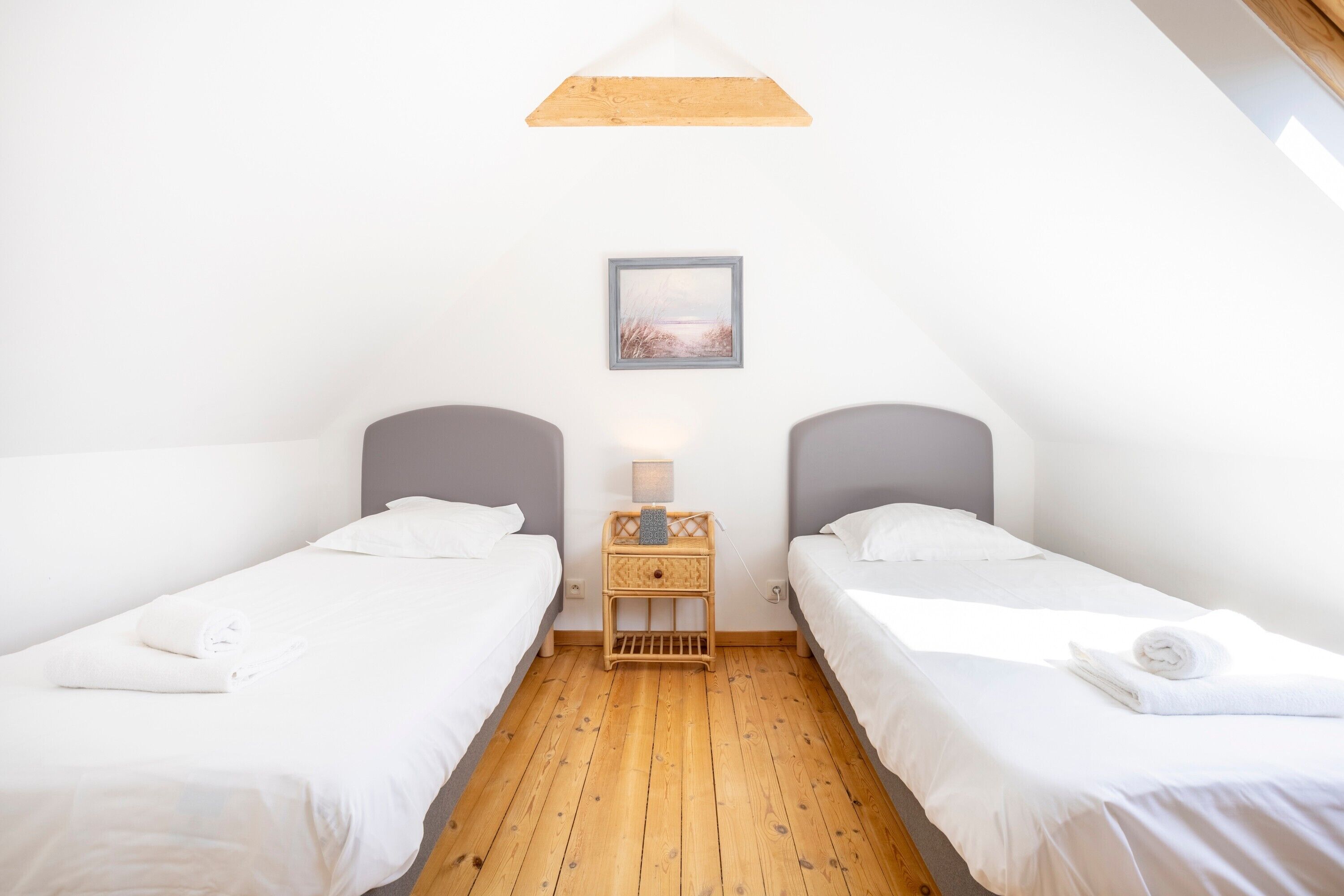 Een slaapkamer met twee bedden, een nachtkastje met een lamp, en een lijst met een afbeelding aan de muur.