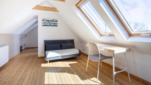 A loft bedroom with a sloped ceiling, wooden beams, a bed, a desk, and skylights.