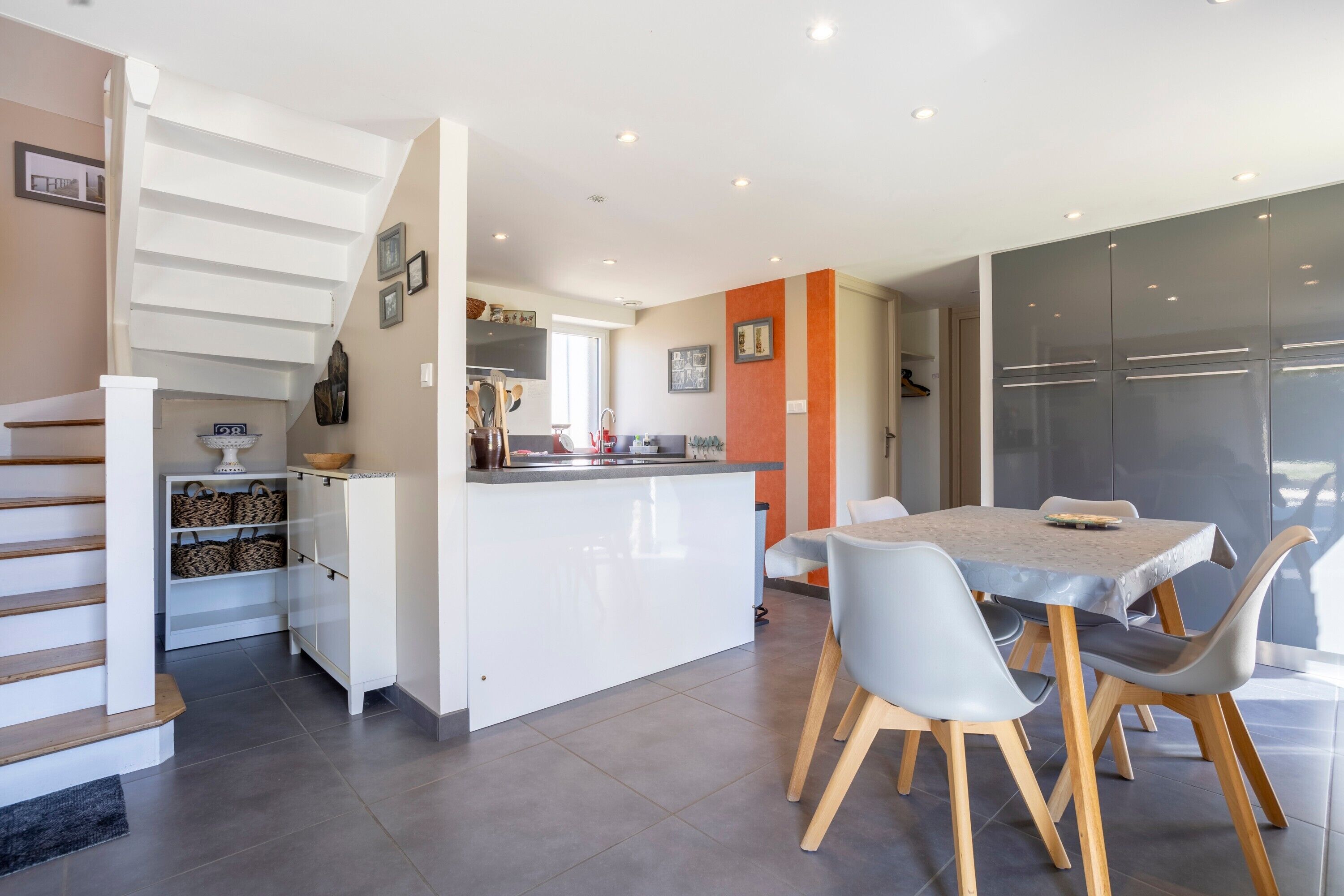 A modern kitchen with a central island, a dining area with a table and chairs, and a staircase leading to a loft bedroom.