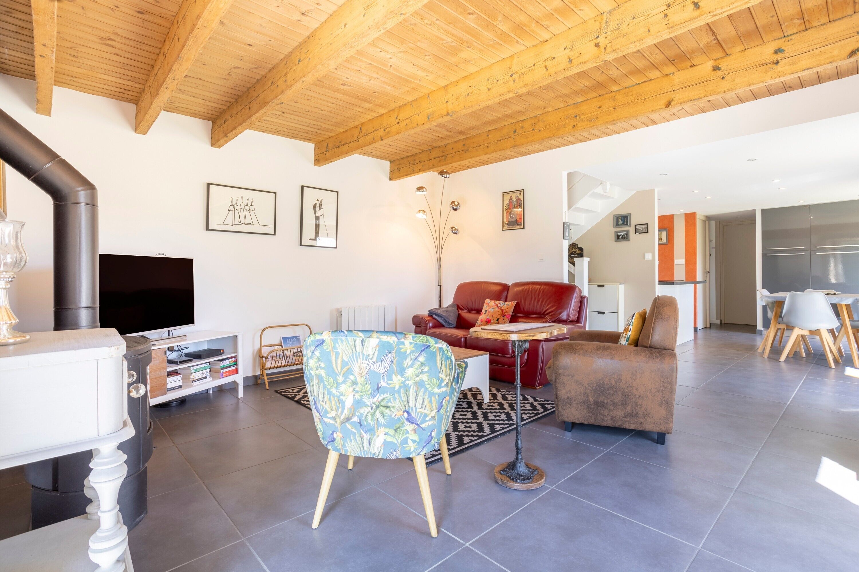 Een moderne woonkamer met een open haard, houten balken in het plafond, een flatscreen televisie en een eethoek.