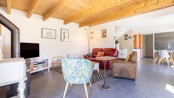 Een moderne woonkamer met een open haard, houten balken in het plafond, een flatscreen televisie en een eethoek.