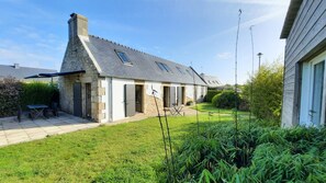 A house with a stone facade, a sloped roof, and a small garden with a table and chairs.