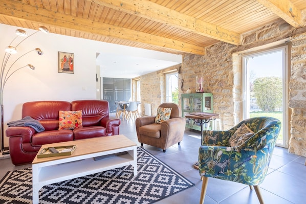 A living room with a red leather sofa, a brown armchair, a patterned rug, and a wooden ceiling.