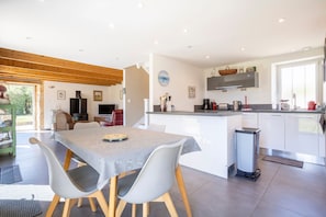 A modern kitchen with a dining area, wooden ceiling beams, and a large window.