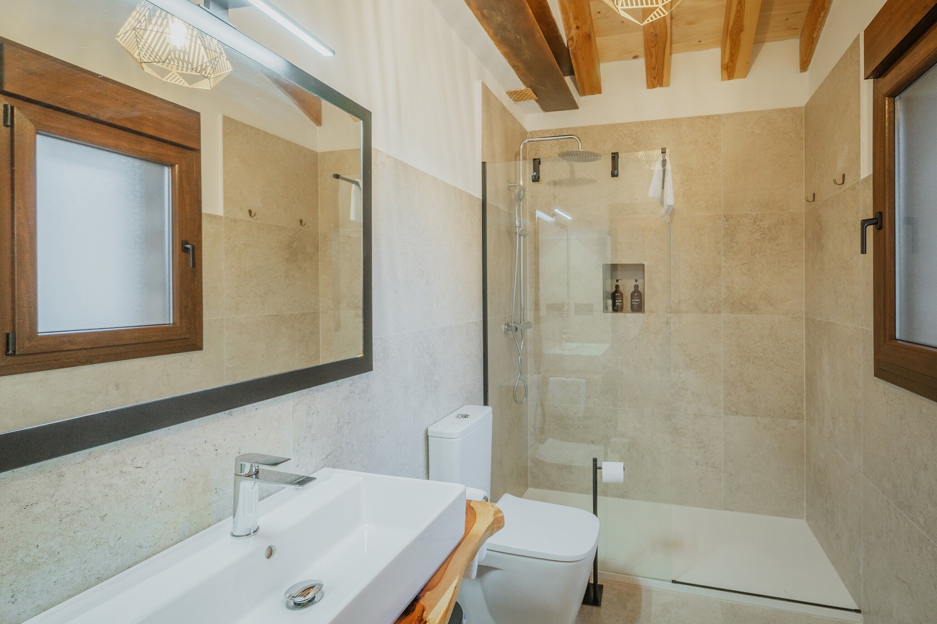 A modern bathroom with a large mirror, a white sink, a toilet, and a glass-enclosed shower area.
