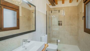 A modern bathroom with a large mirror, a white sink, a toilet, and a glass-enclosed shower area.