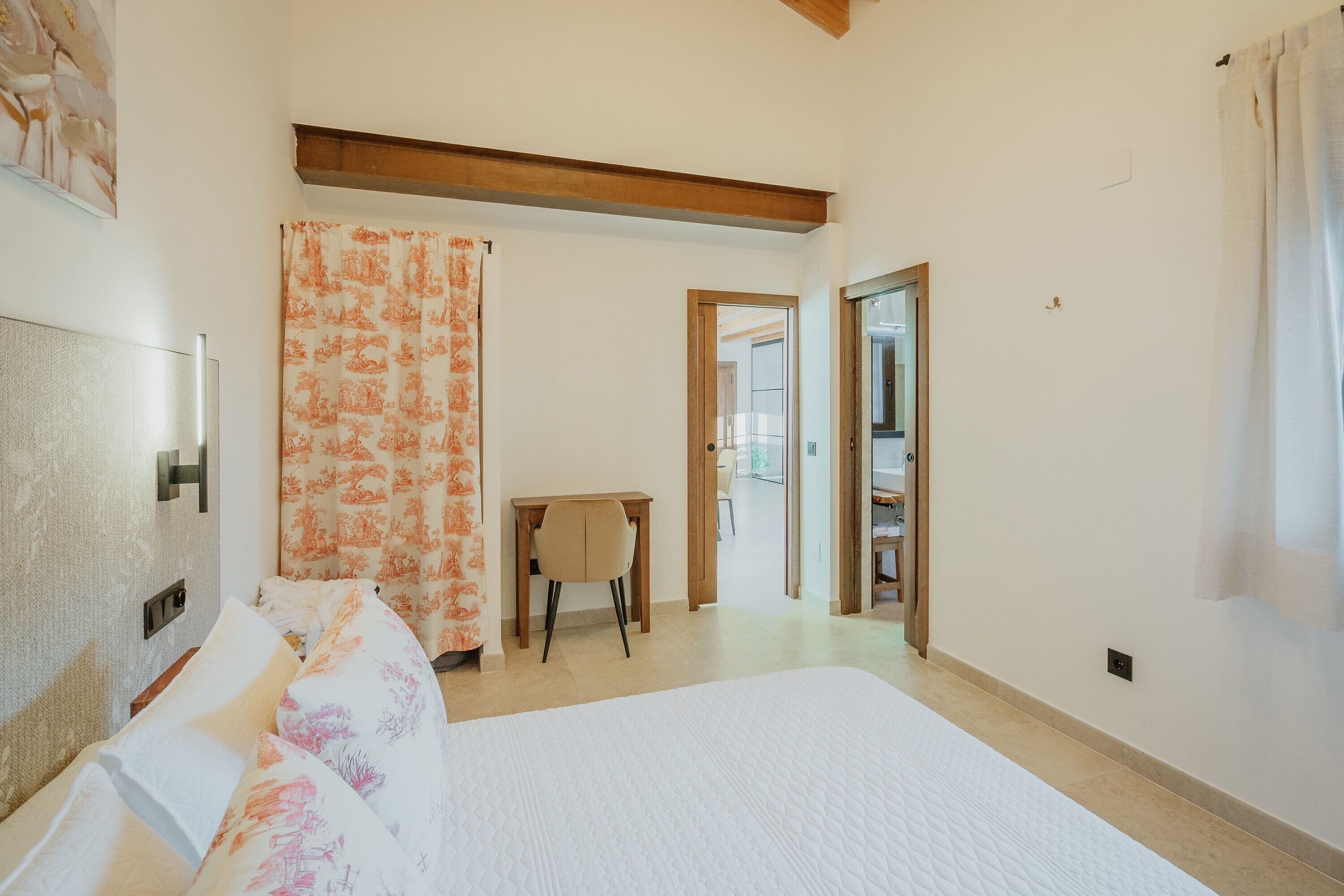 Een slaapkamer met een bed, een bureau en een stoel. Er is een deur die naar een andere kamer leidt.