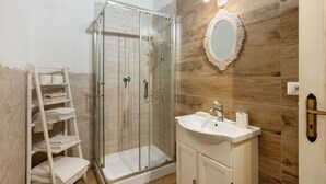 Ein Badezimmer mit einer gläsernen Duschkabine, einem weißen Waschbecken und einer Holzwand.