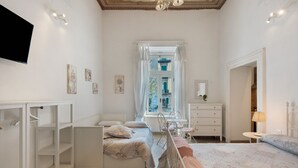 Ein Schlafzimmer mit einem Bett, einem Schreibtisch, einem Stuhl, einer Kommode und einem an der Wand befestigten Fernseher.