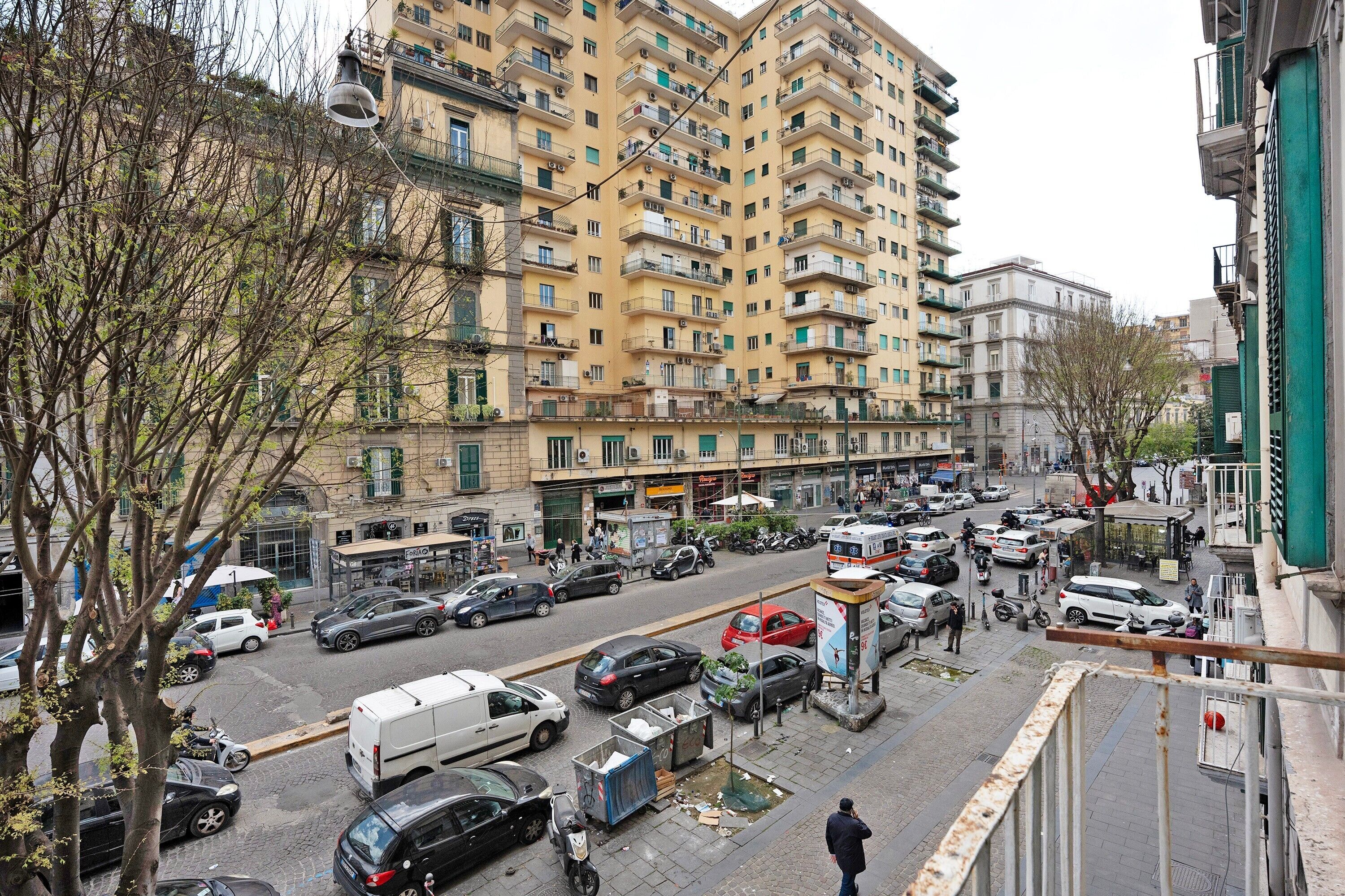 Ein mehrstöckiges Wohngebäude mit Balkonen, eine Straße mit parkenden Autos und ein Fußweg.