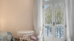 Una habitación con cama, una mesa redonda con una silla, una ventana con cortinas y vista a la calle.