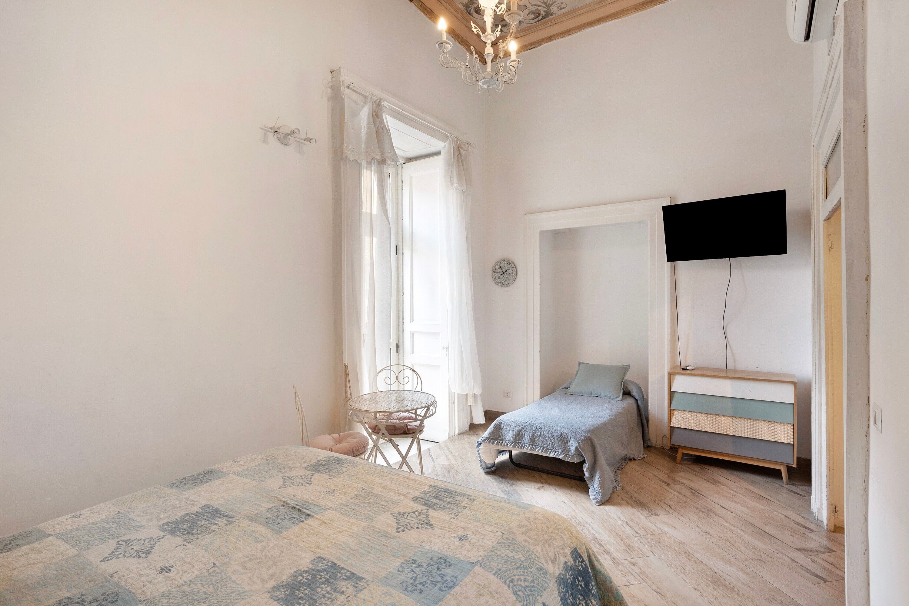 Una camera da letto con un letto, un tavolino rotondo, una cassettiera, una televisione a parete e una finestra con tende.