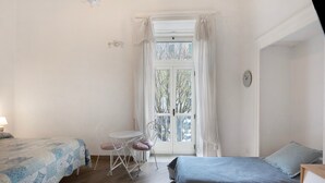 Un dormitorio con dos camas, una mesita, una silla y un ventanal con cortinas.