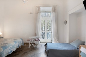 A bedroom with two beds, a small table, a chair, and a window with curtains.