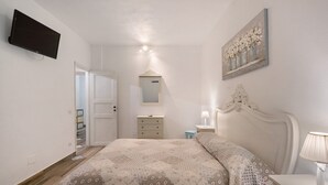 Ein Schlafzimmer mit Bett, Nachttisch, Kommode, Fernseher und einem Bild an der Wand.