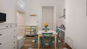 Eine kleine Küche mit Essbereich, weißen Schränken, einem Fernseher auf einem Schrank und einer Vase mit Blumen auf dem Tisch.