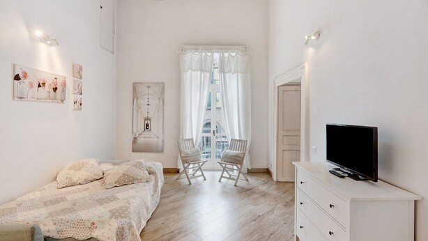 A bedroom with a bed, two chairs, a TV on a dresser, and a window with curtains.