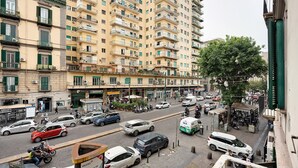 A multi-story building with balconies, a street with cars and scooters, and a sidewalk with a sign.