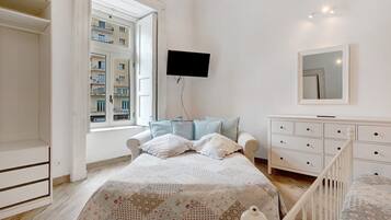 A bedroom with a bed, a dresser, a TV, and a window with a view of buildings.