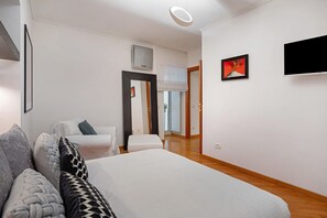 A modern hotel room with a large bed, a sitting area with a sofa and armchairs, a flat-screen TV, and a large window. - Apartment 'Incantevole Dimora In Zona Chiaia' with Balcony, Wi-Fi and Air Conditioning (Naples)