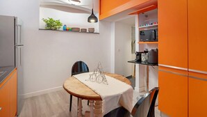 A compact kitchen with a dining table, a hanging light fixture, and a microwave.
