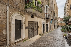 A narrow cobblestone street with old buildings, a closed metal gate, and a parked car.
