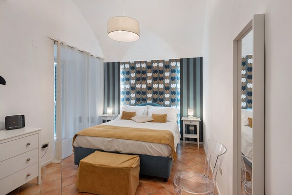 Un dormitorio con cama, mesitas de noche, escritorio, silla, lámpara colgante y espejo.